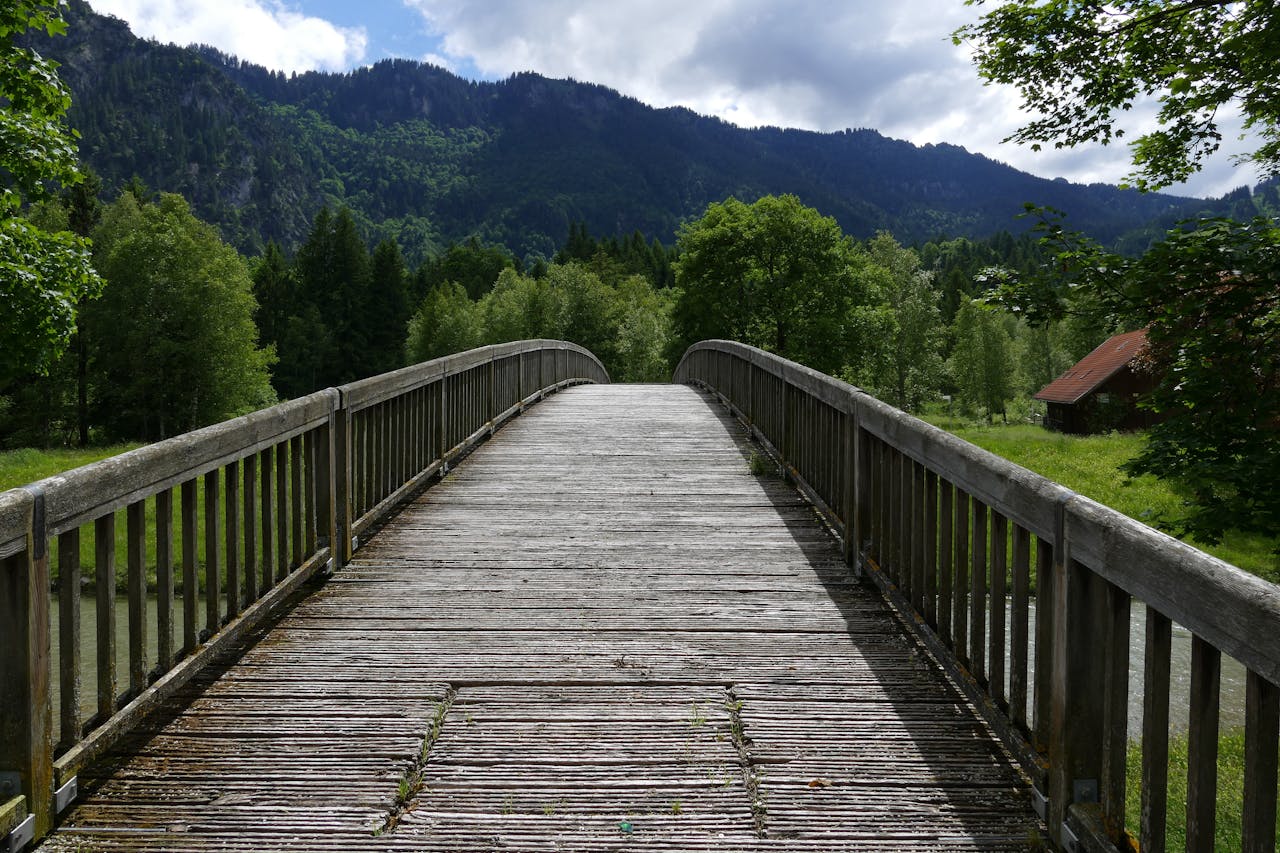 portfolio-img-04 A serene wooden bridge amidst lush greenery and mountains, perfect for a peaceful nature walk.