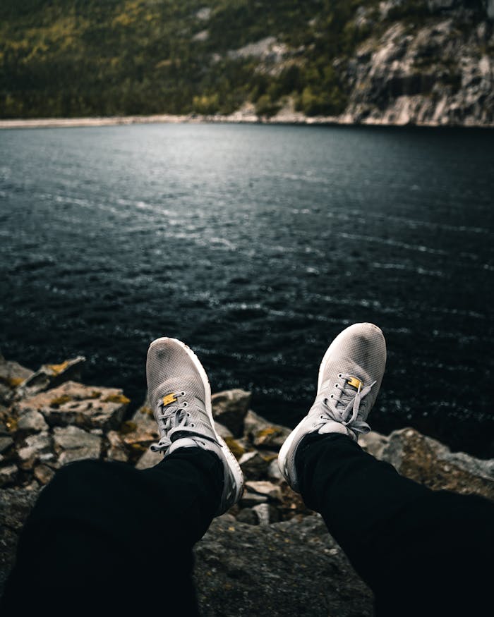 Feet in sneakers rest near a serene mountain lake, embracing nature's tranquility.