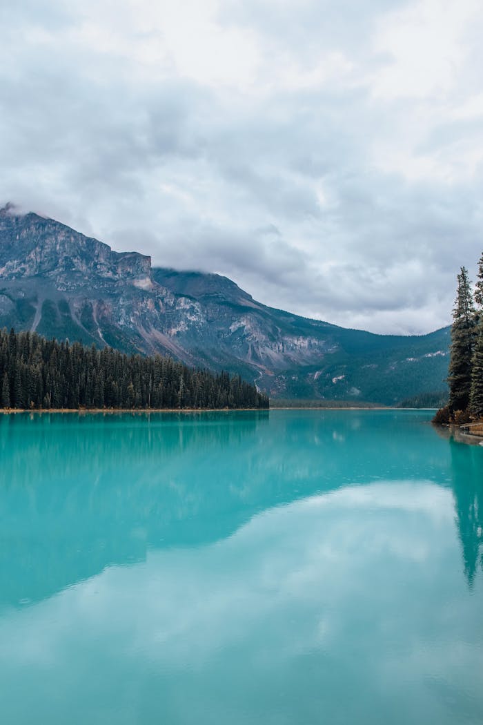 Stunning turquoise mountain lake with forest reflection under cloudy sky.